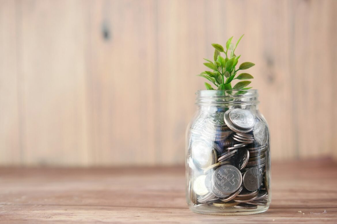 Glaskrukke med mønter og en spirende plante som symbol på langsigtet, passiv opsparing