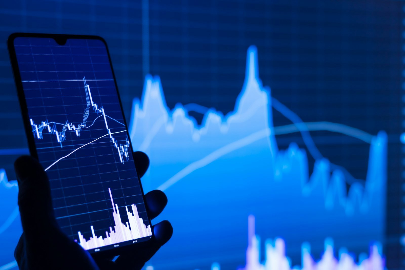 Shorting af aktier: person holder telefon foran faldende aktiekurs